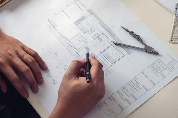 Beskåret billede af arkitekt, der holder pen med tegning på skrivebordet