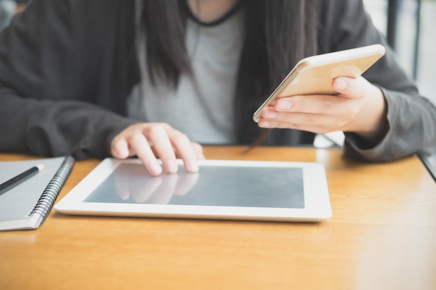 Beskåret billede af kvinde, der bruger smartphone og digital tablet ved bordet