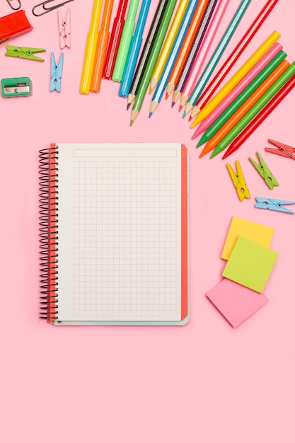 blank open graph paper notebook and school utensils on a pink background with copy space