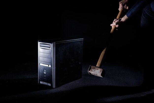 Blow of a large heavy hammer with a long handle onto a desktop computer isolated on a black