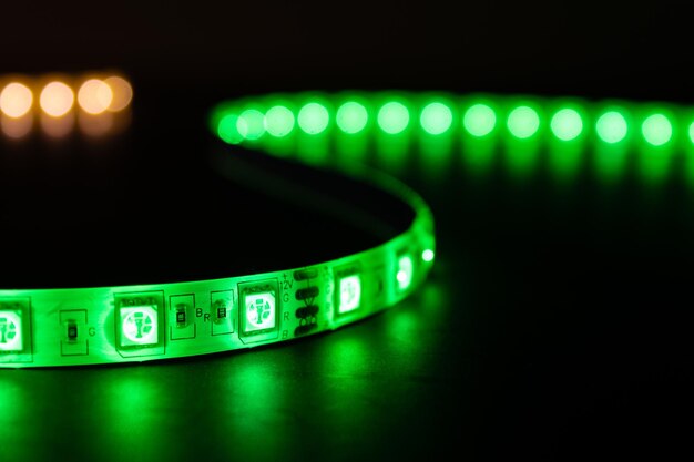 Bobbin with roll of glowing LED strip lighting placed on table green and warm white color