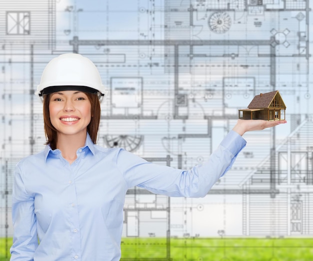 building, developing, advertising and architecture concept - friendly young smiling businesswoman in white helmet holding house on palm