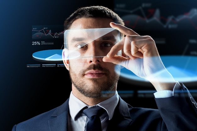 business, augmented reality and modern technology concept - businessman working with transparent smartphone and virtual charts projections over black background