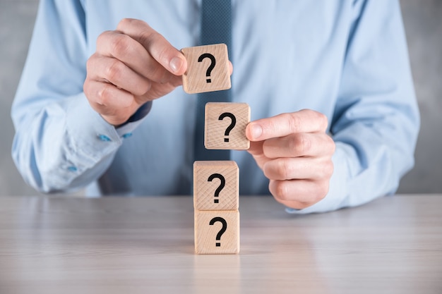 Businessman hold and put wooden cube block shape with question marks on grey table