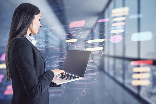 Businesswoman holding a laptop in an office corridor colorful blockchain schemes in the background Cryptocurrency and trading concept