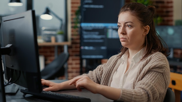 Caucasian system engineer working focused looking at computer screen while typing in big data server room. Software developer writing code with algorithms compiling on screens in background.