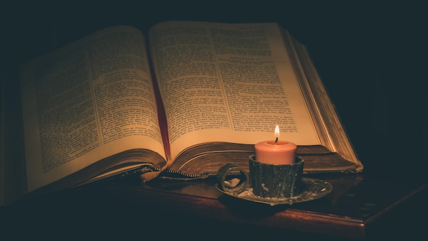 Close-up of lit candle and bible on table in darkroom