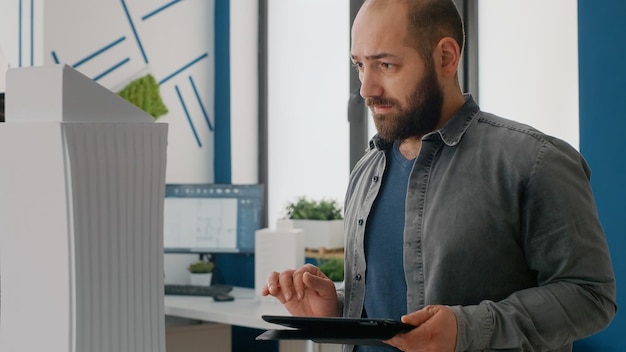 close up of man architect using digital tablet to design building model and layout in office. expert contractor working with device to plan construction project and urban structure.
