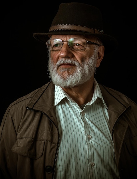 close-up of senior man wearing hat against black background