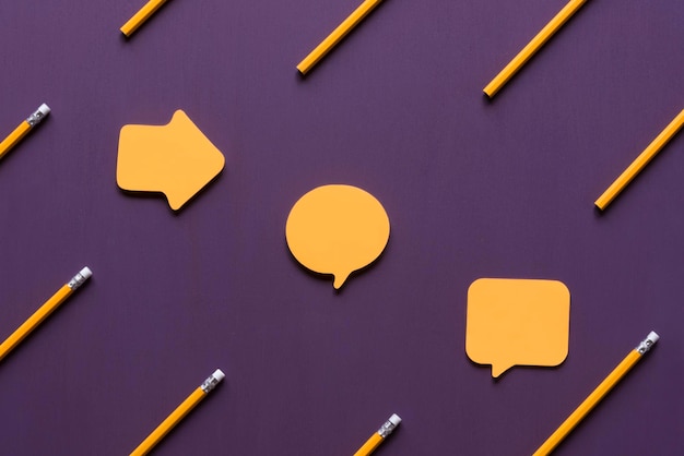 Close-up of yellow pencils and speech bubbles on purple table