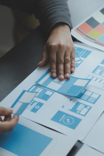 Close up ux developer and ui designer brainstorming about mobile app interface wireframe design on table with customer breif and color code at modern officeCreative digital development agency
