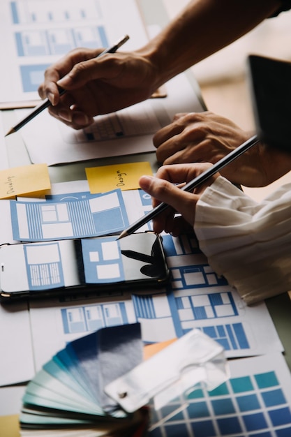 Close up ux developer and ui designer brainstorming about mobile app interface wireframe design on table with customer breif and color code at modern officeCreative digital development agency