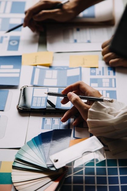 Close up ux developer and ui designer brainstorming about mobile app interface wireframe design on table with customer breif and color code at modern officeCreative digital development agency