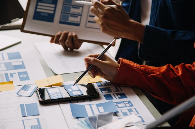 Close up ux developer and ui designer brainstorming about mobile app interface wireframe design on table with customer breif and color code at modern officeCreative digital development agency