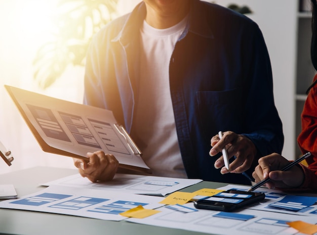 Close up ux developer and ui designer brainstorming about mobile app interface wireframe design on table with customer breif and color code at modern officeCreative digital development agency