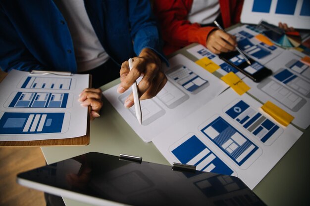 Close up ux developer and ui designer brainstorming about mobile app interface wireframe design on table with customer breif and color code at modern officeCreative digital development agency