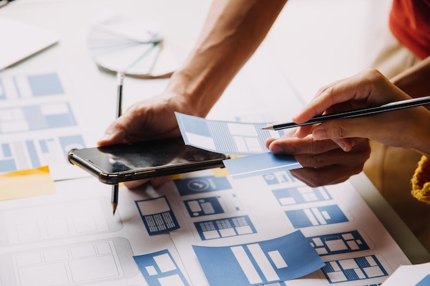 Close up ux developer and ui designer brainstorming about mobile app interface wireframe design on table with customer breif and color code at modern officeCreative digital development agency