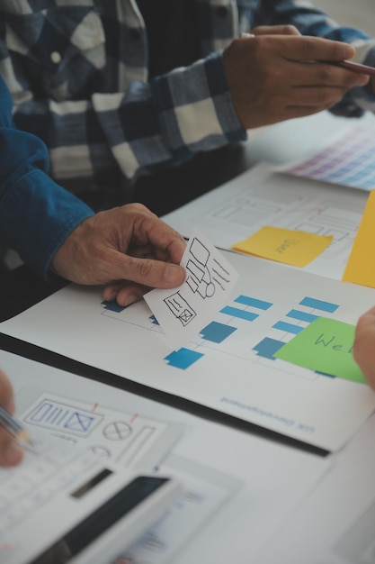 Close up ux developer and ui designer brainstorming about mobile app interface wireframe design on table with customer breif and color code at modern officeCreative digital development agency