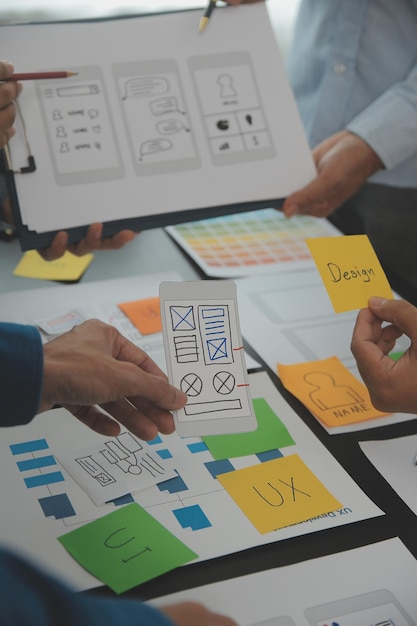 Close up ux developer and ui designer brainstorming about mobile app interface wireframe design on table with customer breif and color code at modern officeCreative digital development agency