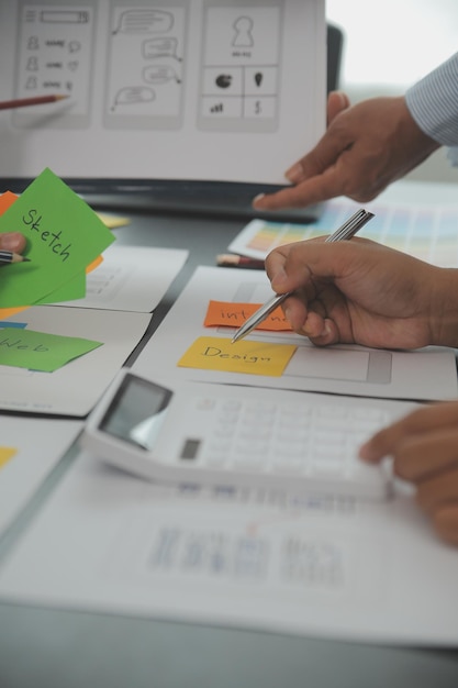 Close up ux developer and ui designer brainstorming about mobile app interface wireframe design on table with customer breif and color code at modern officeCreative digital development agency