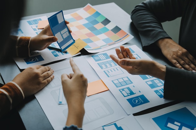 Close up ux developer and ui designer brainstorming about mobile app interface wireframe design on table with customer breif and color code at modern officeCreative digital development agency
