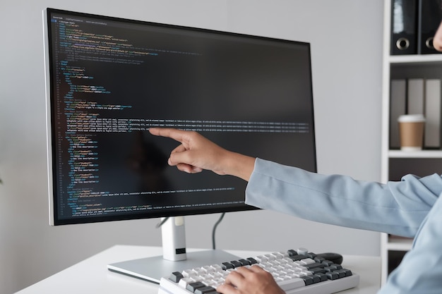 Close up view of programmer pointing to desktop computer with developing programming code trying to solve the problem