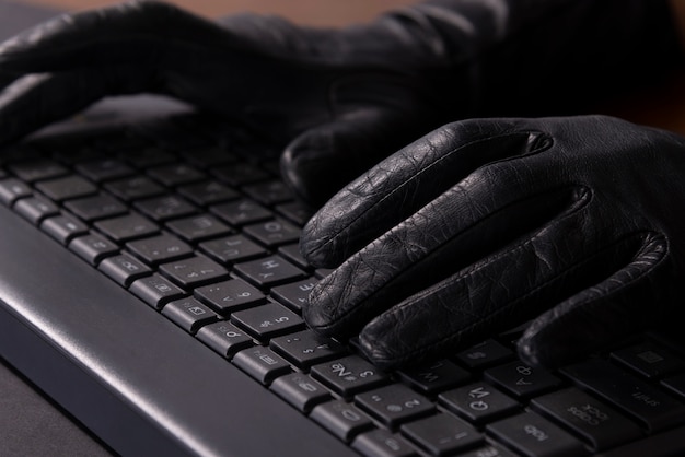 Cyberkriminelles hænder i handsker på bærbar computer tastatur.