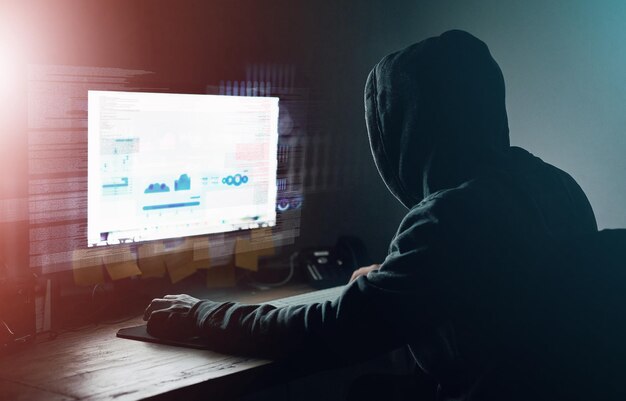 Dark office and man at computer for hacking online programming and cybersecurity at night Software developer or hacker in hoodie coding for password firewall or network access for cyber attack