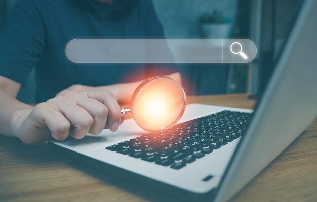 Data Search Technology Search Engine Optimization Mans hands are using magnifying glass on computer keyboard A computer notebook to Searching for information on website Button on virtual screen