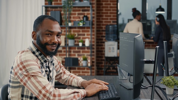 Database programer writing code and smiling while coworker walks by holding clipboard in it agency. Relaxed app developer typing on keyboard with colleagueas computing big data.