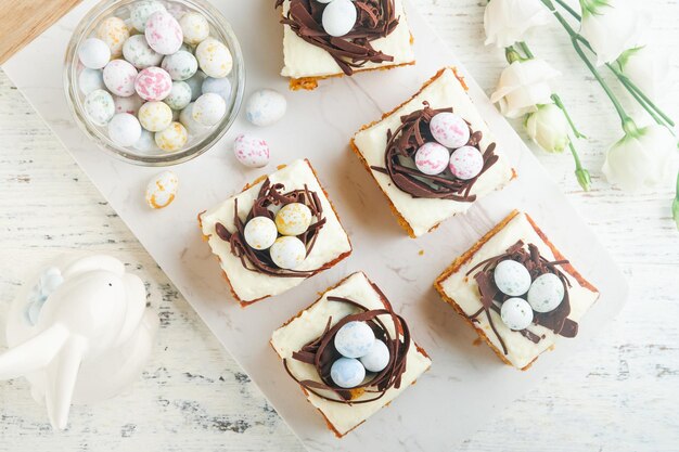 Easter carrot cake bars decorated with chocolate nest and chocolate candy eggs blossoming cherry or apple flowers on rustic light wooden backgrounds Easter holiday meal Traditional Easter food