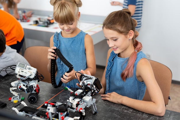 Education, children, technology, science and people concept - group of happy kids with laptop computer building robots at robotics school lesson