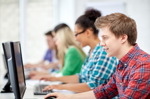 education, people, friendship, technology and learning concept - group of happy international high school students or classmates in computer class