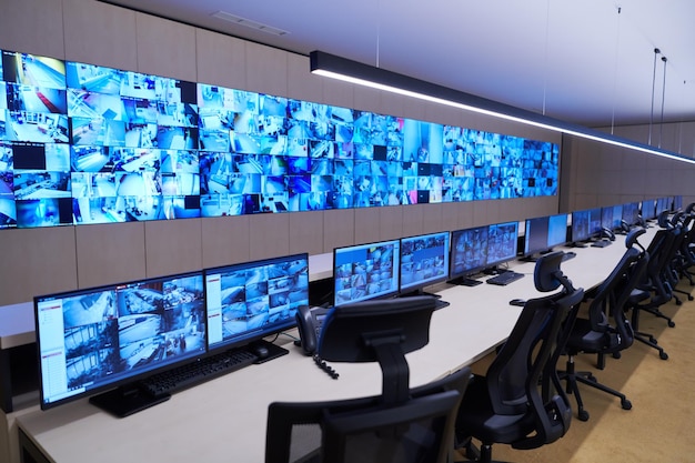 Empty interior of big modern security system control room, workstation with multiple displays, monitoring room with at security data center  Empty office, desk, and chairs at a main CCTV security data