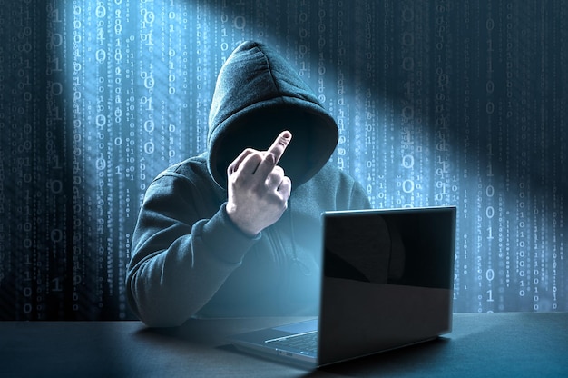 Faceless hooded hacker showing middle finger gesture meaning of fuck Computer hacker in hoodie Data thief internet fraud darknet and cyber security concept