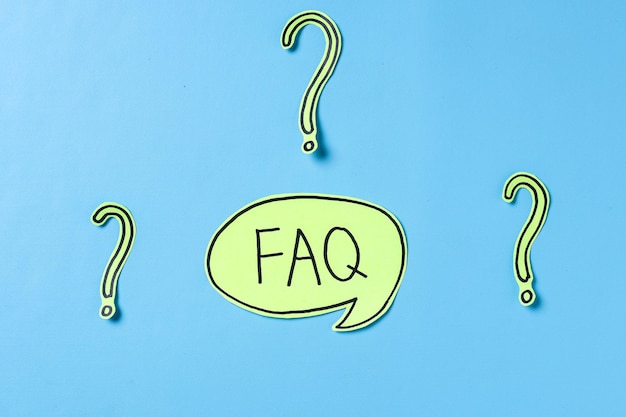 FAQ-tekst skrevet på sticky note og spørgsmålstegn på papir på blå baggrund