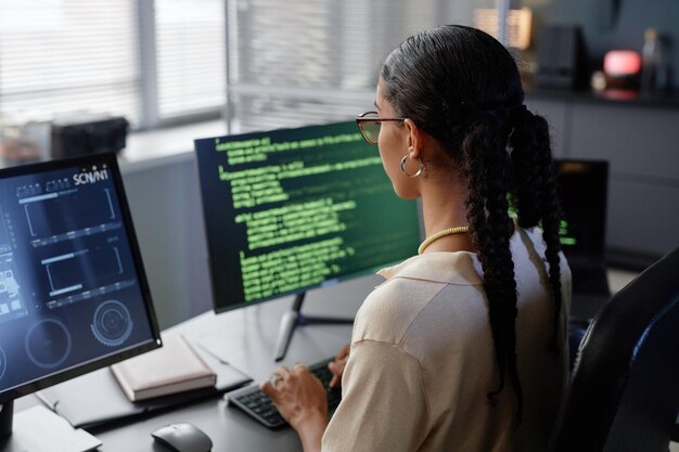 Female it developer with glasses looking at multiple computer screens working in office