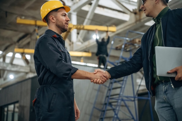 Friendly handshake Two male factory workers are in the warehouse