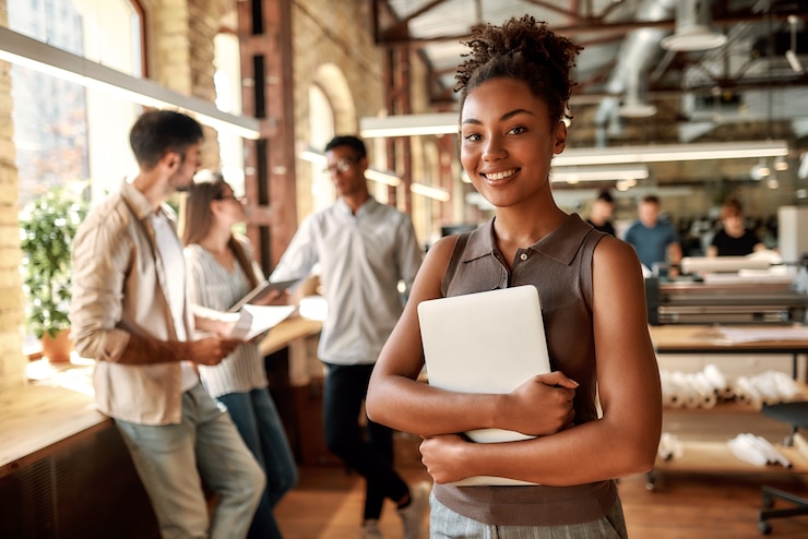 Foto glad for at arbejde her ung og glad afroamerikansk kvinde, der holder en bærbar computer og smiler, mens hun står