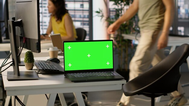 Green screen laptop on desk in workspace with admins in background