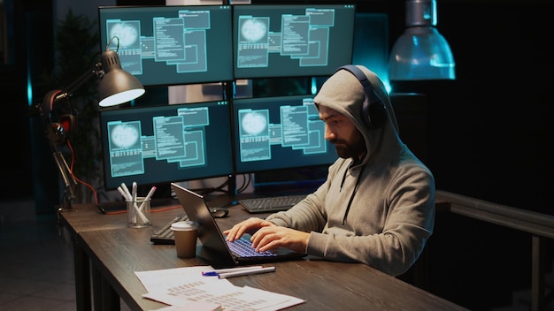 Hacker coder hacking system at night using virus to produce computer malware and server error. Data thief stealing information from software app, working with multiple monitors. Handheld shot.