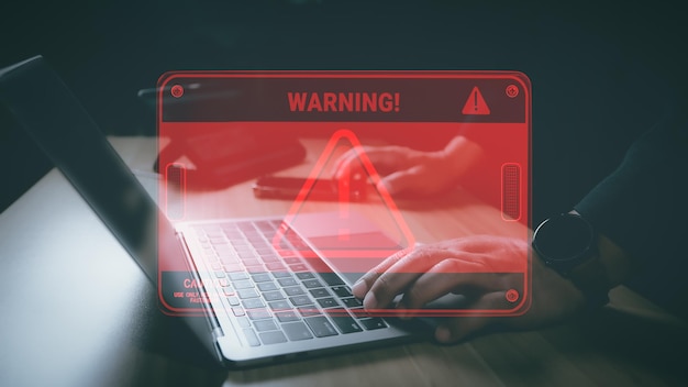 Hacker or programmer using laptop with triangle caution warning sign coding cryptography hacker crime virus for notification error and maintenance concept Computer with red warning sign