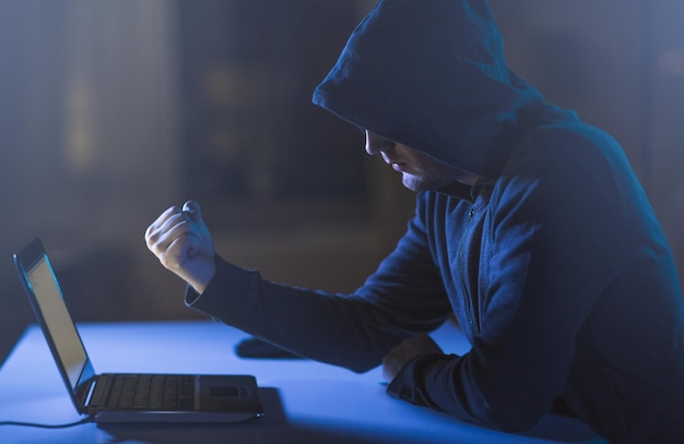 hacker showing fist to laptop in dark room