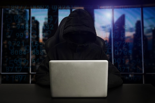 Hacker using computer with digital interface while sitting at desk of blurry interior Hacking and thief concept