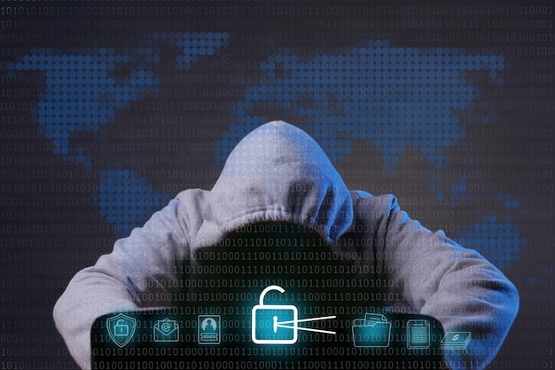 Hacker wearing grey hoodie using laptop computer in the dark