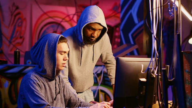 Hacking group leader teaching new member how to steal valuable data by taking advantage of security breaches Script kiddie in underground hideout learns how to gain unauthorized access to systems