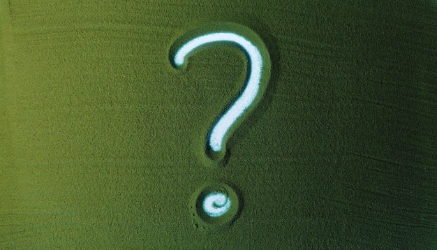 Hand drawing question mark symbol in the green sand male hand writes a symbol on the green sand with