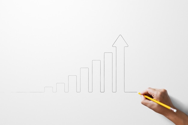 Hand holding yellow colour pencil sketch outline arrow graph growing on white paper background Business target development or investment financial profit stock market and goal achievement on economy
