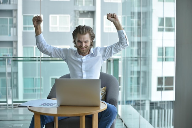 Happy businessman using laptop while sitting at office