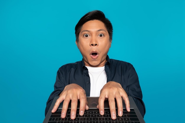 Happy chinese guy in casual chatting at laptop keyboard at social networks